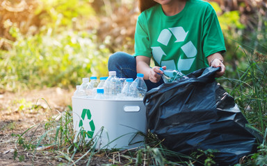 A woman picking up garbage plastic bottles into a box and plastic bag for recycling concept