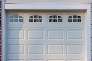 Double car classic insulated steel raised panel garage door framed with a white trim to add accent, with transom light windows divided by muntins on a new American home - obrazy, fototapety, plakaty