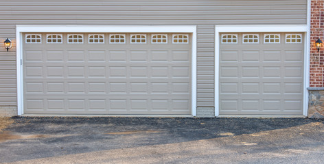 Two car and single car charcoal gray classic insulated steel raised panel garage door framed with a white trim to add accent, with transom light windows divided by muntins on a new American home - obrazy, fototapety, plakaty