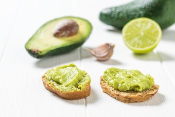 Lime and avocado with two slices of bread with guacamole on a wooden table. Diet vegetarian Mexican food avocado.