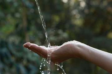 Water pouring on hand with blurred nature background.