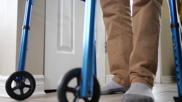 At home, a disabled older man walking with a walker slowly helped by the rollator walking frame.
