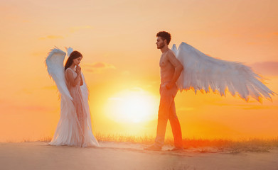 Fototapeta na wymiar artistic processing. Two divine angels man and woman go to meet each other. design white costume wings. Girl with loose long hair brunette. Backdrop bright sunny sunset in fabulous natural sand desert