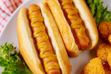 Hot dog with mustard on white plate with lettuce.