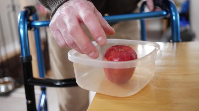 Shaking hands of a disabled man trying to grab an apple but ending dropping it on the ground. Parkinson disease concept of living with the illness at home.