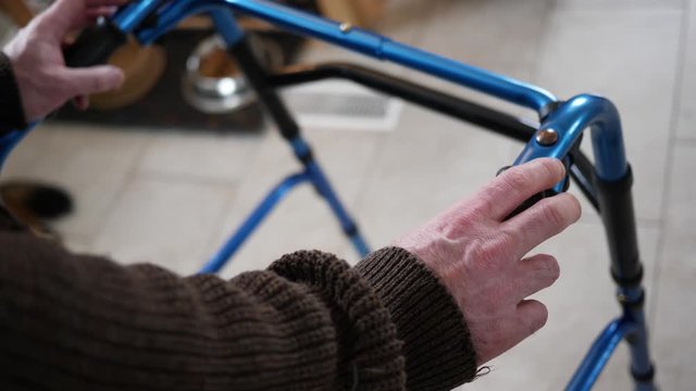 At home, a disabled older man walking with a walker slowly helped by the rollator walking frame.