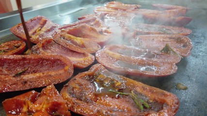 The cook puts slices of red bell pepper on a hot stove. Dousing vegetables with vegetables,