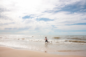 Fototapeta na wymiar Boy running on beach splashing in the waves