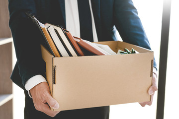 Sad Fired Young Employee businessmen hold boxes including pot plant and documents for personal...