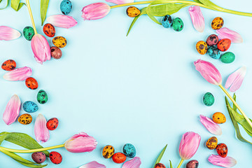 Stylish background with colorful easter eggs isolated on blue background with pink tulip flowers. Flat lay, top view, mockup, overhead, template