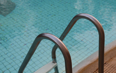 Closeup of stainless handrail of ladder at  swimming pool with water surface background.