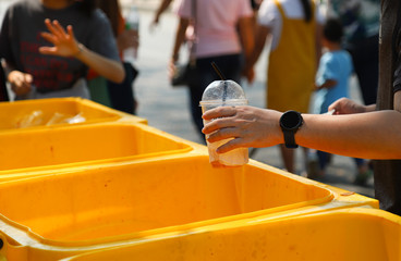 Closeup of man's hang dropping garbage into yellow litter bin.