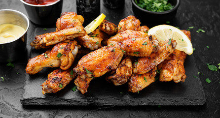 Baked chicken wings served with different sauces and lemon. Black background