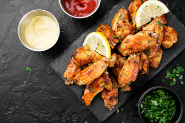 Baked chicken wings served with different sauces and lemon. Black background