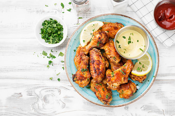 Baked chicken wings served with different sauces and lemon. White wooden background