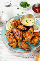 Baked chicken wings served with different sauces and lemon. White wooden background