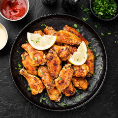 Baked chicken wings served with different sauces and lemon. Black background