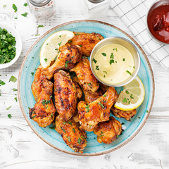 Baked chicken wings served with different sauces and lemon. White wooden background