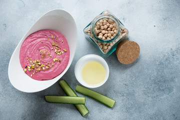 Hummus with addition of beetroot served in a bowl with cucumber slices, flatlay on a light-blue stone background with space