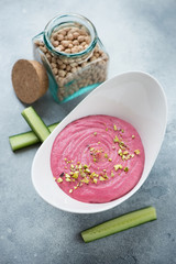 Bowl of hummus with beetroot and cucumber slices on a light-blue stone background, vertical shot, elevated view