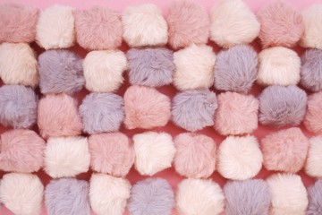 Pompons fur background.  fluffy gray, pink, beige pompons on a pink background.  texture of the pompons. Fluffy fur background in pastel colors.