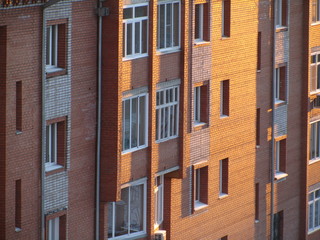 Fototapeta na wymiar Modern brick residential building close-up. Perspective view of a house wall with windows and balconies. Facade of a brick urban apartment building.