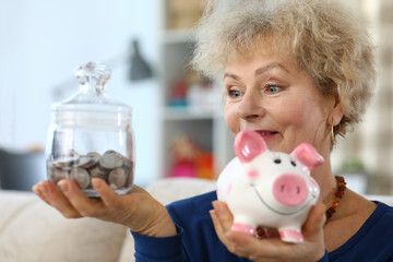 An old lady holding piggy bank and glass jar coins. Accumulation pension capital. Pay off all debts and loans. Woman first puts off then spends. Initial savings fund. Expenses include food