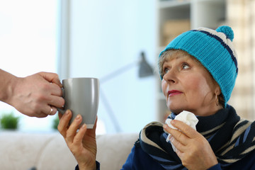 Cold elderly lady in knitted hat takes cup tea. Side effects drugs. Cold medicine for elderly....