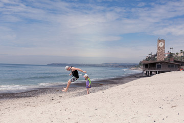 A dad is playing a sand jumping game with his kids at the beach.