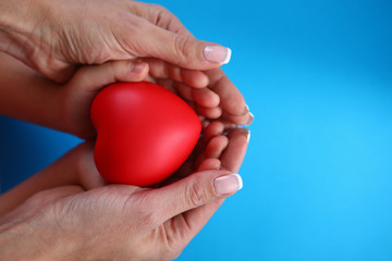 Close-up in female palms childrens hands and heart. Timely diagnosis facilitates treatment. Prevention cardiovascular diseases in family. Healthier heart mother and baby. Healthy heart protection