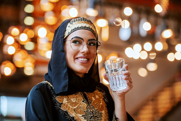 Gorgeous positive muslim woman in traditional wear with beautiful smile sitting in coffee shop...