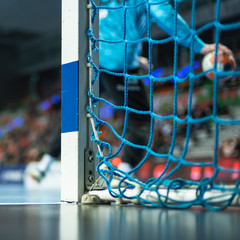 Detail of handball goal post with net and handball match in the background.