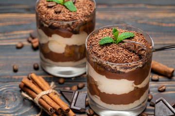 Classic tiramisu dessert in a glass cup and pieces of chocolate on wooden background