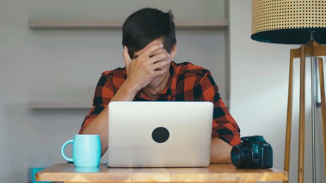 Sad man photographer crying during his work at laptop at home. Creative crisis concept.