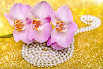 purple Orchid and pearl necklace on a shiny gold background.
