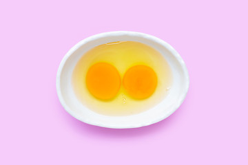 Two egg yolk and white in a bowl on pink background.