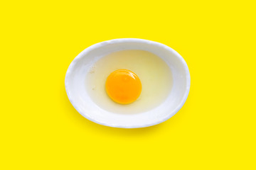 Egg yolk and white in a bowl on yellow background.