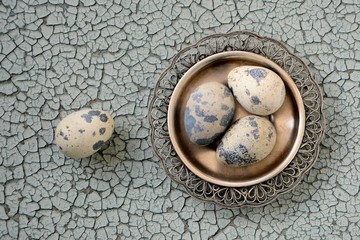 Quail eggs on a silver plate on an old cracked blue background close up