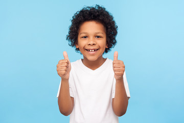 Like! Portrait of happy little boy with curly hair in white T-shirt smiling at camera and doing...