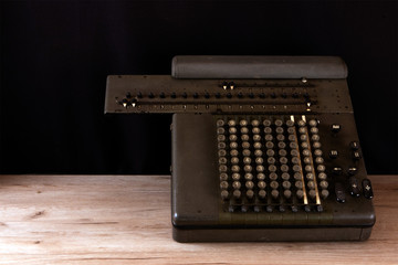 Old counting mechanism, dusty vintage arithmometer standing on a wooden board against black fabric