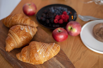 Big croissants, berries, red apples on a wooden table