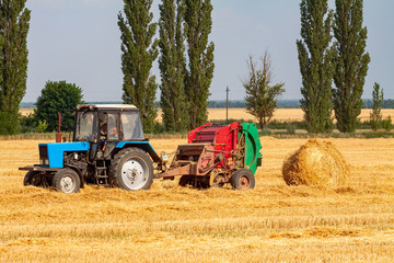 tractor makes big straw roll on yellow field at summer day