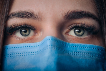 Close-up of pretty assistant wearing in a blue mask looking at camera. Woman wearing mask and...
