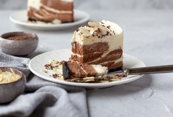 A bite and a piece of homemade raw chocolate cheesecake or mousse cake on white plate decorated with almond flakes and chocolate chips