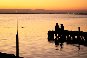 Naklejka na ściany i meble a couple on a pier watching the sunset on a lake 