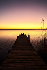 a couple on a pier watching the sunset on a lake 