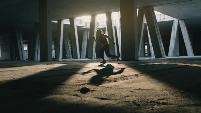Athletic woman doing reverse lunge to single leg jump in urban area. Shot in slow motion with sunlight and concrete pillars in background.