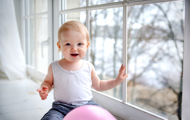 white girl sits on the floor near the window and smiles, kid, baby  with a pink ball