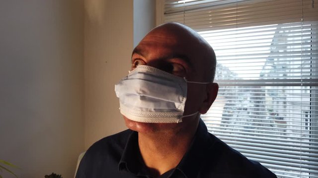 Confused man wearing medical face mask to protect from spreading coronavirus outbreak infection in a semi-dark room