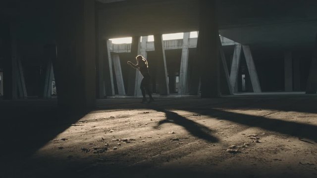 Woman doing shadow boxing workout in urban area. Shot in slow motion with sunlight and concrete pillars in background.